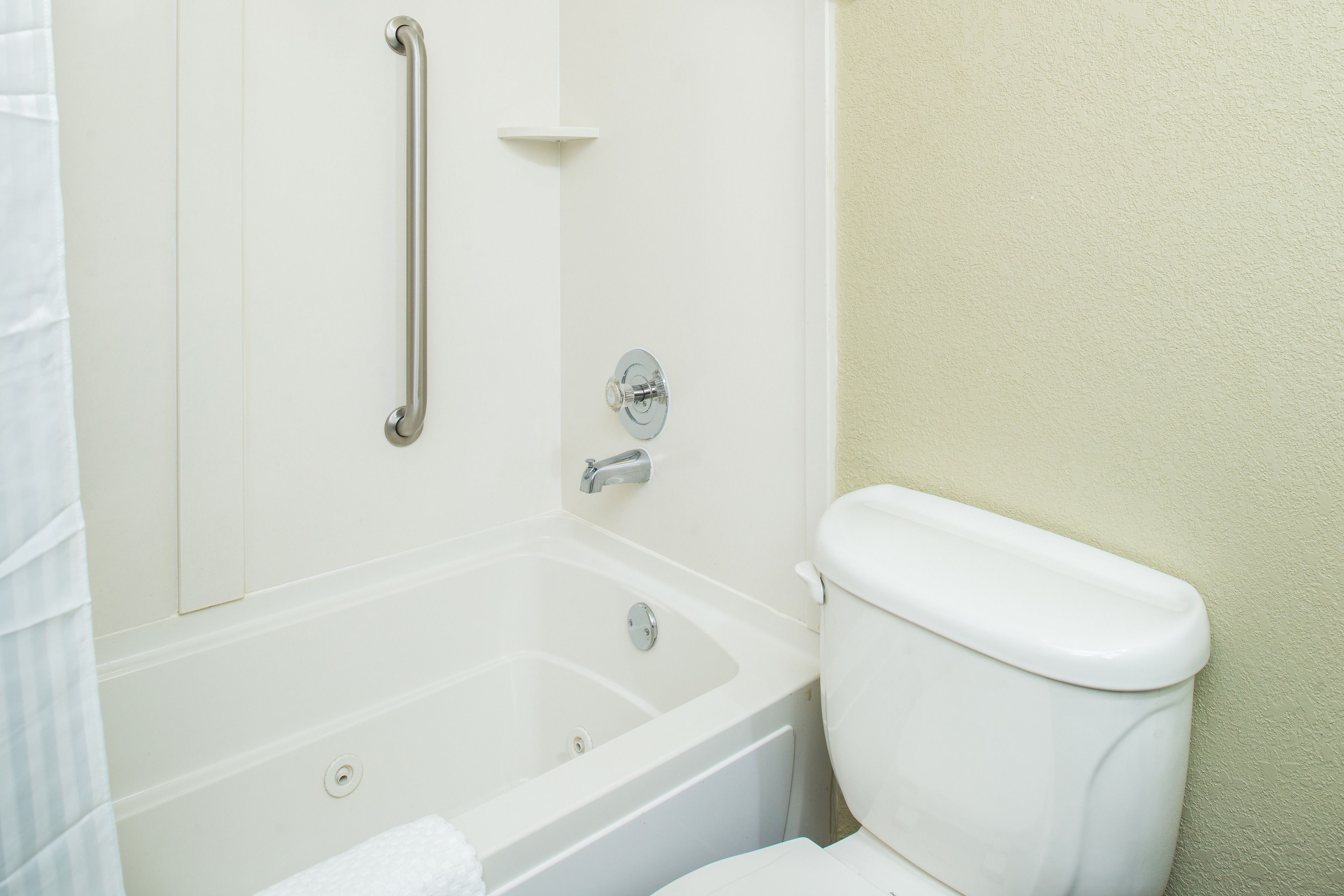 A bathroom with a bathtub, toilet, and a grab bar.
