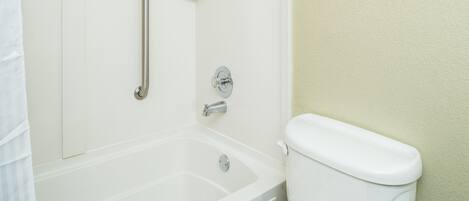 Un baño con bañera, inodoro y barra de apoyo.