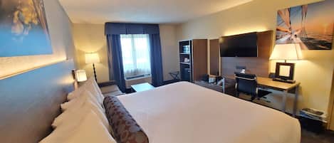 A hotel room with a large bed, a desk with a chair, a TV, and a wardrobe.