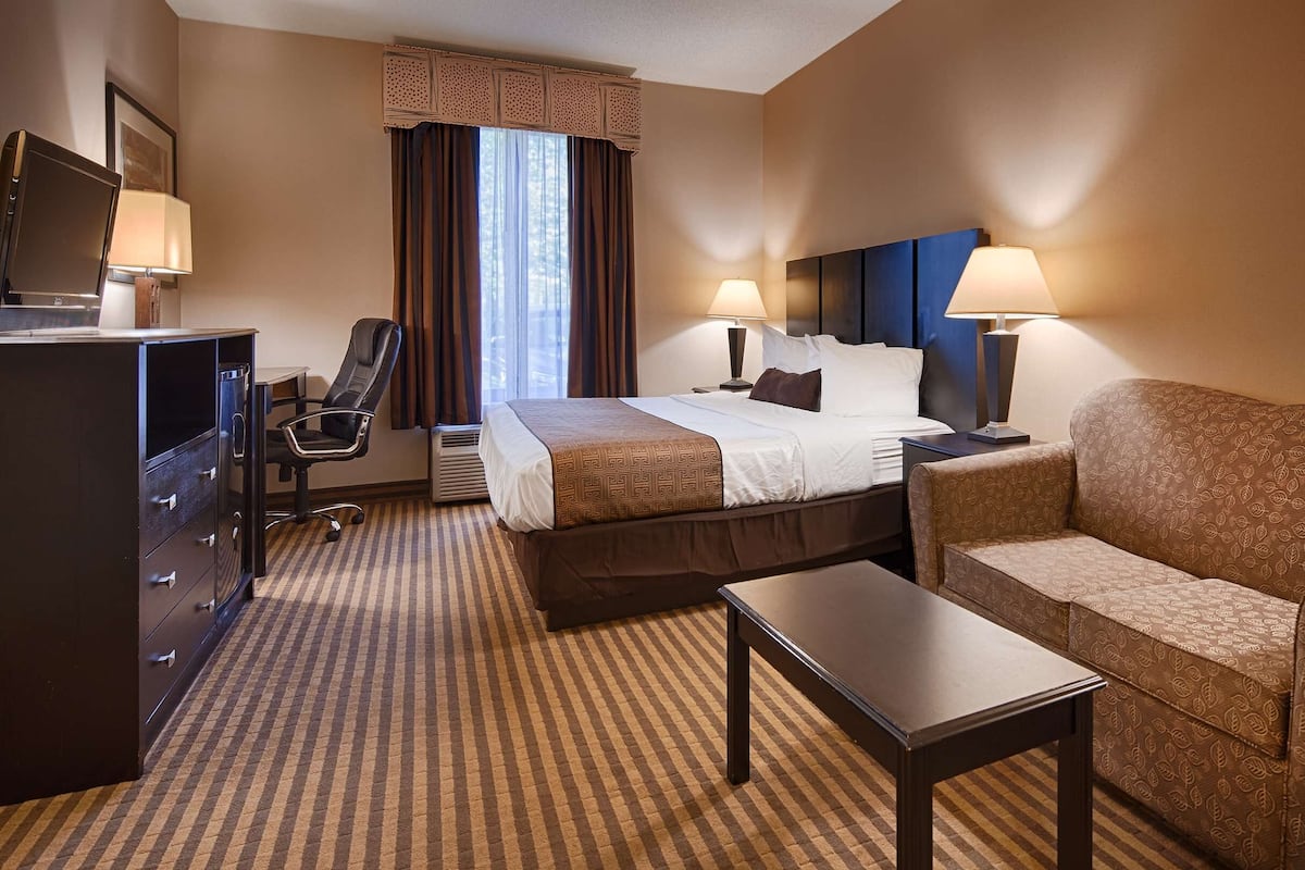 A hotel room with a bed, a desk, a chair, a sofa, and a TV.