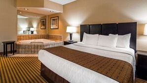 A hotel room with a large bed, a separate bathroom with a bathtub, a mirror, and a small table.