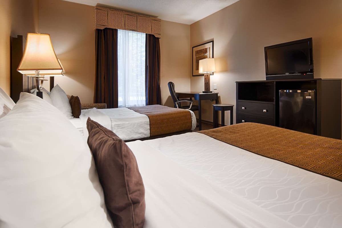 A hotel room with two beds, a desk, a chair, a television, and a refrigerator.