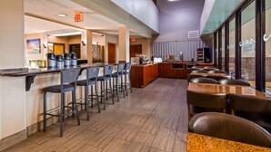 A modern bar area with high stools and a counter, equipped with coffee machines and a TV.