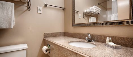 A bathroom with a granite countertop, a sink, a mirror, a towel rack, and a toilet paper holder.