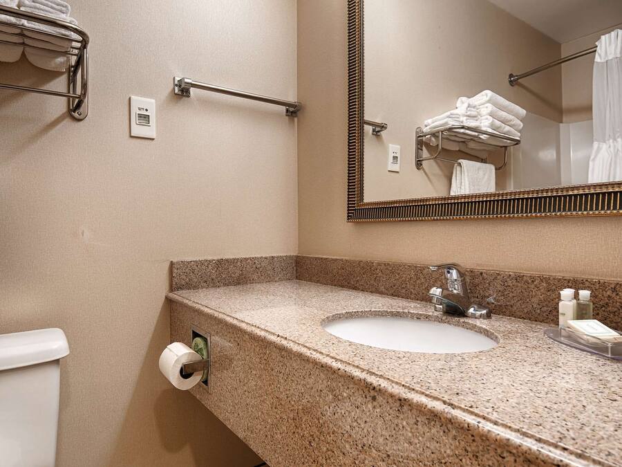 A bathroom with a granite countertop, a sink, a mirror, a towel rack, and a toilet paper holder.