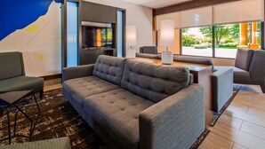 A modern hotel room with a grey sofa, a small table, and a TV.