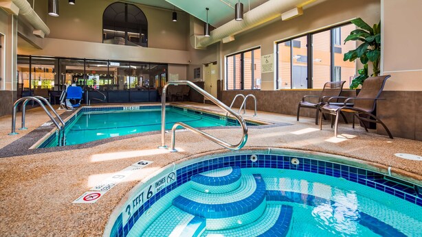 An indoor pool with clear water, a lounge area with chairs, and a pool lift sign.