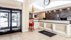 A reception area with a glass door entrance, a clock on the wall, a red cart, and a modern kitchen counter.