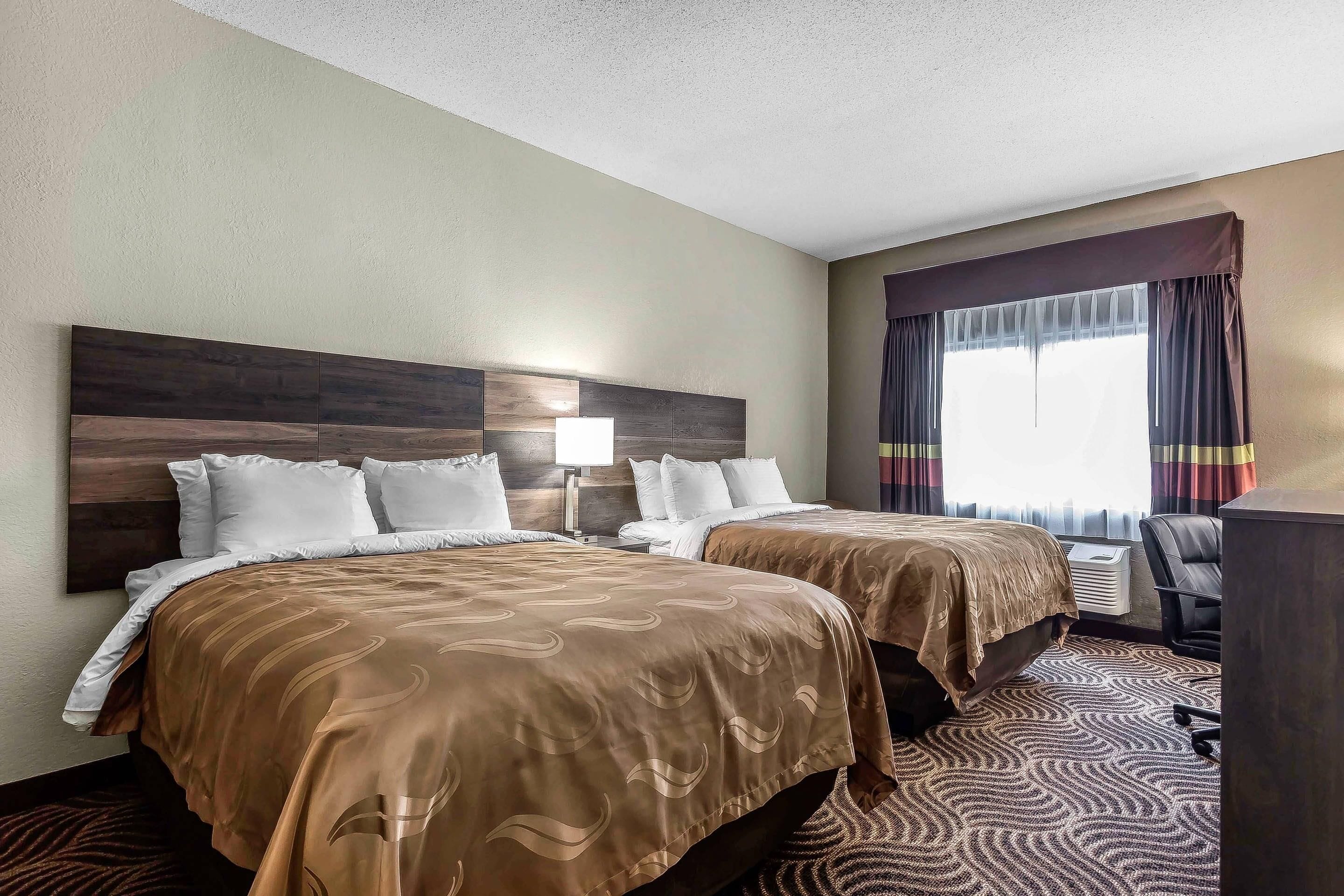 A hotel room with two beds, a desk, and a chair.