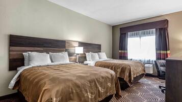 A hotel room with two beds, a desk, and a chair.