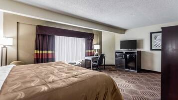 A hotel room with a large bed, a desk with a chair, a television, and a minibar.