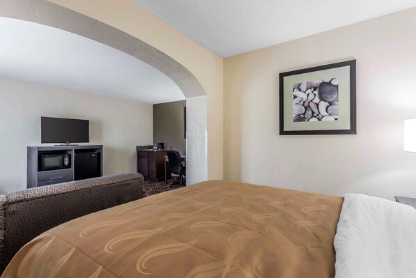 Una habitación de hotel con cama, televisión, kitchenette y una obra de arte enmarcada en la pared.