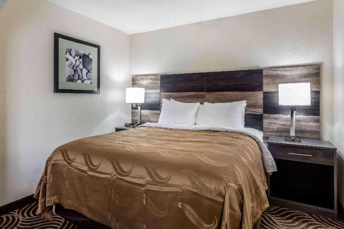 Quarto de hotel com cama, duas mesas de cabeceira, um quadro na parede e um tapete estampado.