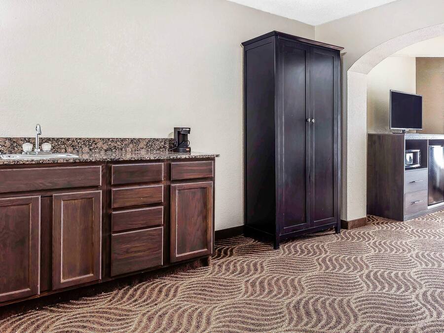 Una habitación de hotel con un mueble de madera oscura, una cafetera y un televisor sobre un pedestal.