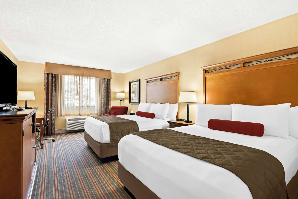 A hotel room with two beds, a desk, a TV, and a window with curtains.