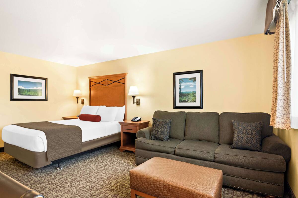 A hotel room with a bed, a sofa, a small table, and two wall-mounted lamps.
