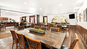 A spacious dining area with wooden tables and chairs, a central island with a moss centerpiece, and a kitchen in the background. - Best Western Newberry Station (La Pine)