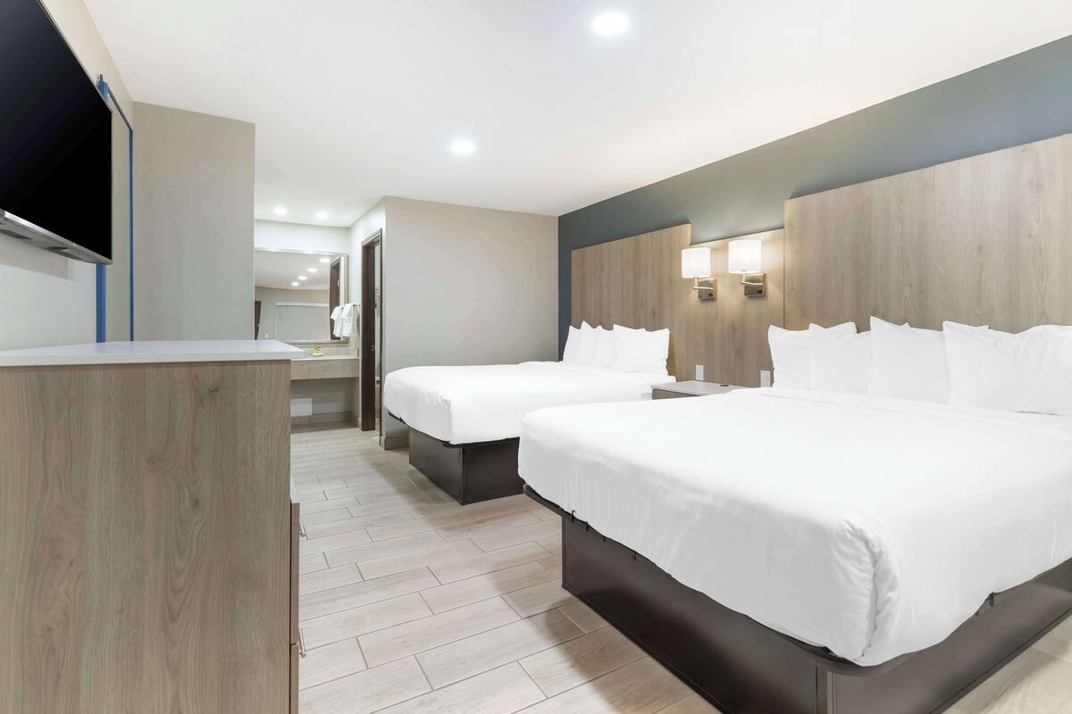 A hotel room with two beds, a TV, and a wooden headboard.