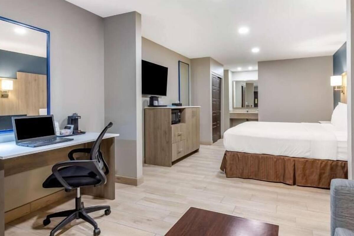 A hotel room with a desk, chair, bed, and a large mirror.