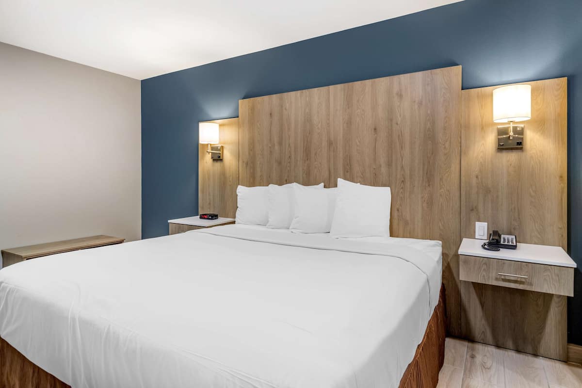 A hotel room with a large bed, wooden headboard, bedside tables, and wall-mounted lamps.