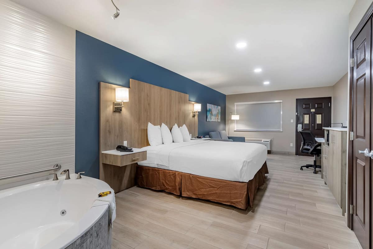 A modern hotel room with a large bed, a separate bathroom with a bathtub, and a desk area.