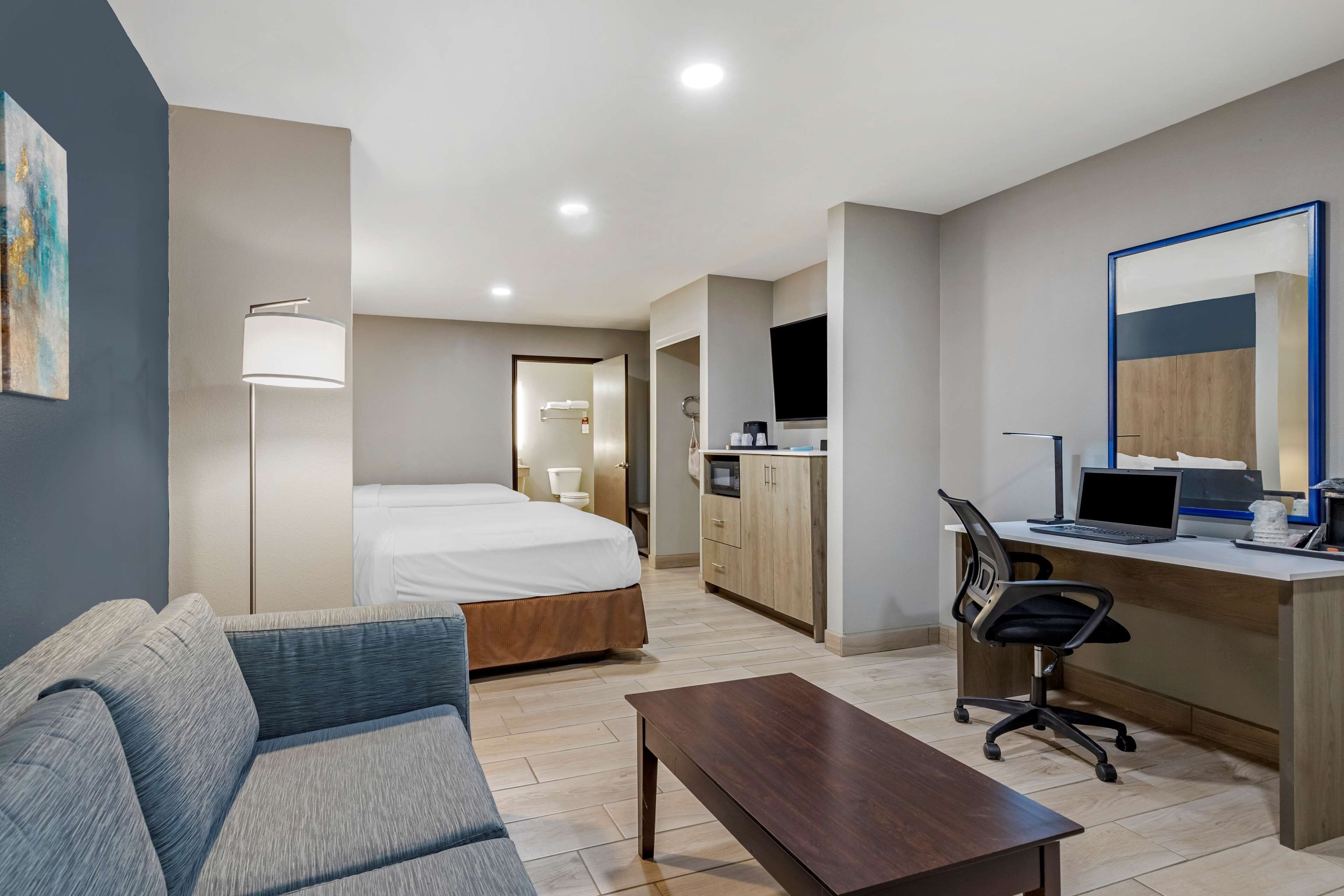 Ein modernes Hotelzimmer mit Bett, einer Couch, einem Schreibtisch mit Computer, einem Fernseher und einer Küchenzeile.