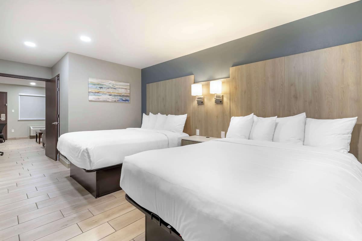 A hotel room with two beds, a wooden headboard, a painting on the wall, and a desk with a chair.