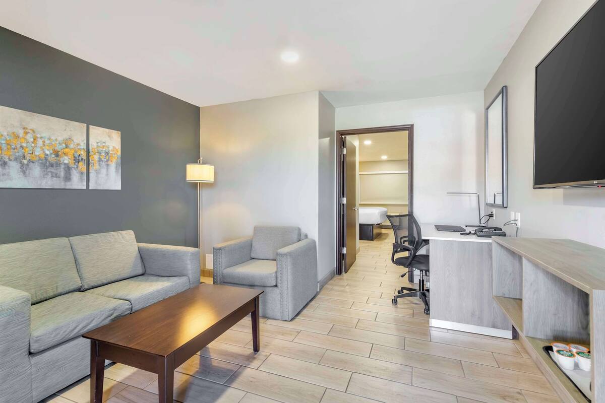 A modern hotel room with a sofa, armchair, desk, and a painting on the wall.