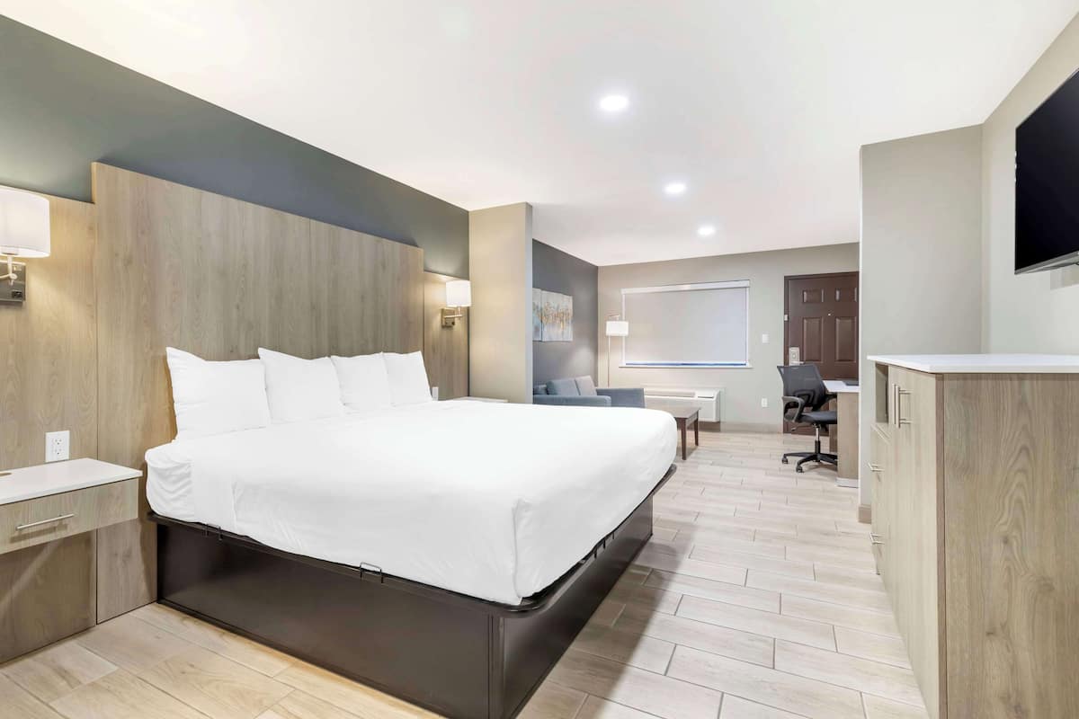 A modern hotel room with a large bed, a desk, a chair, and a TV mounted on the wall.