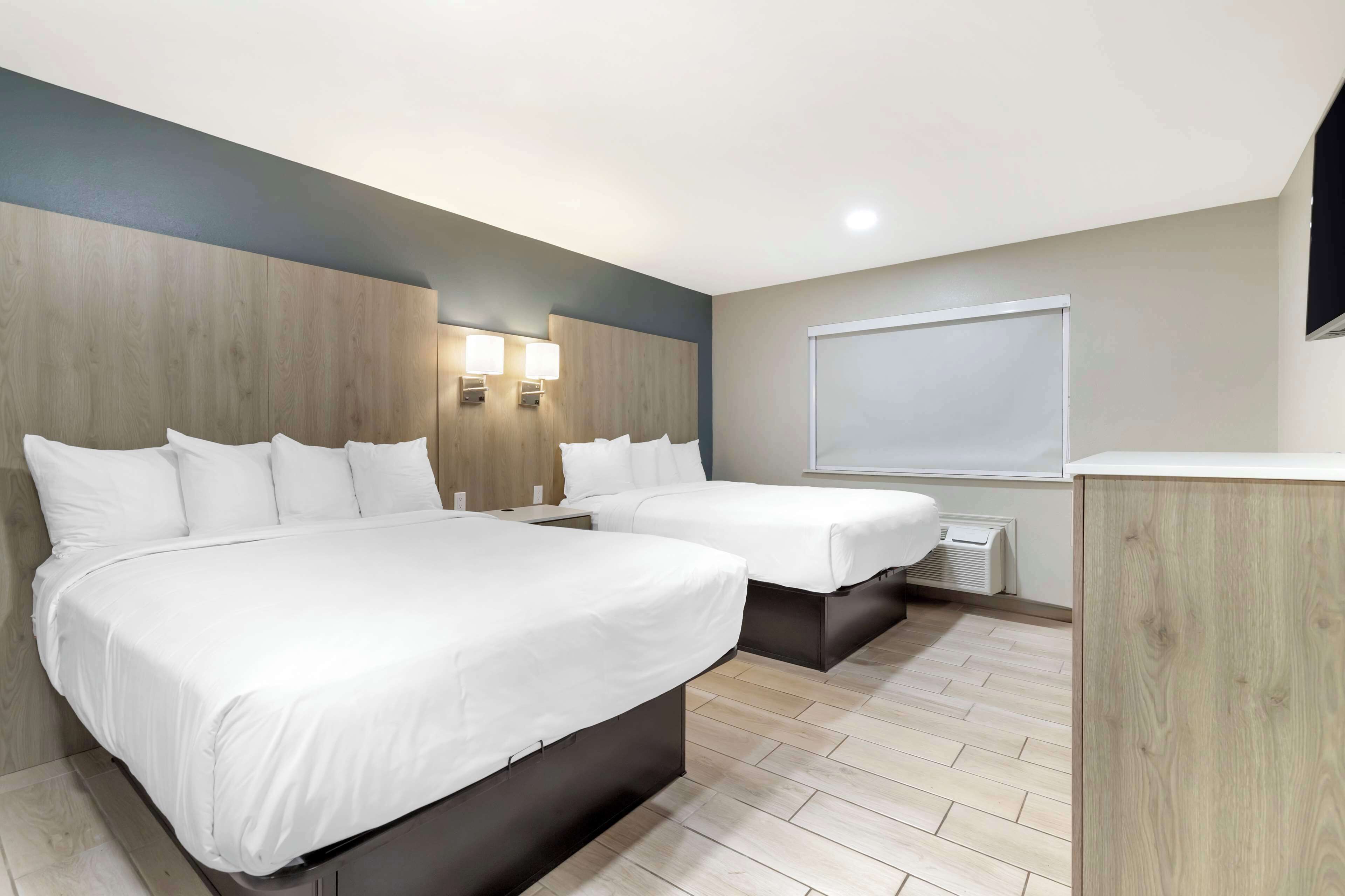 A hotel room with two beds, a wooden headboard, a wall-mounted TV, and a window with a view.