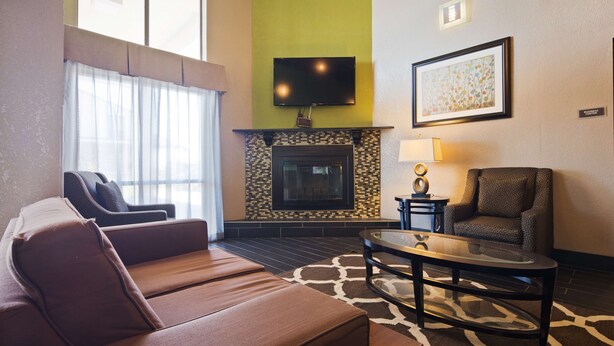 A living room with a sofa, armchair, fireplace, television, and artwork. - Best Western Windsor Inn (Dumas)