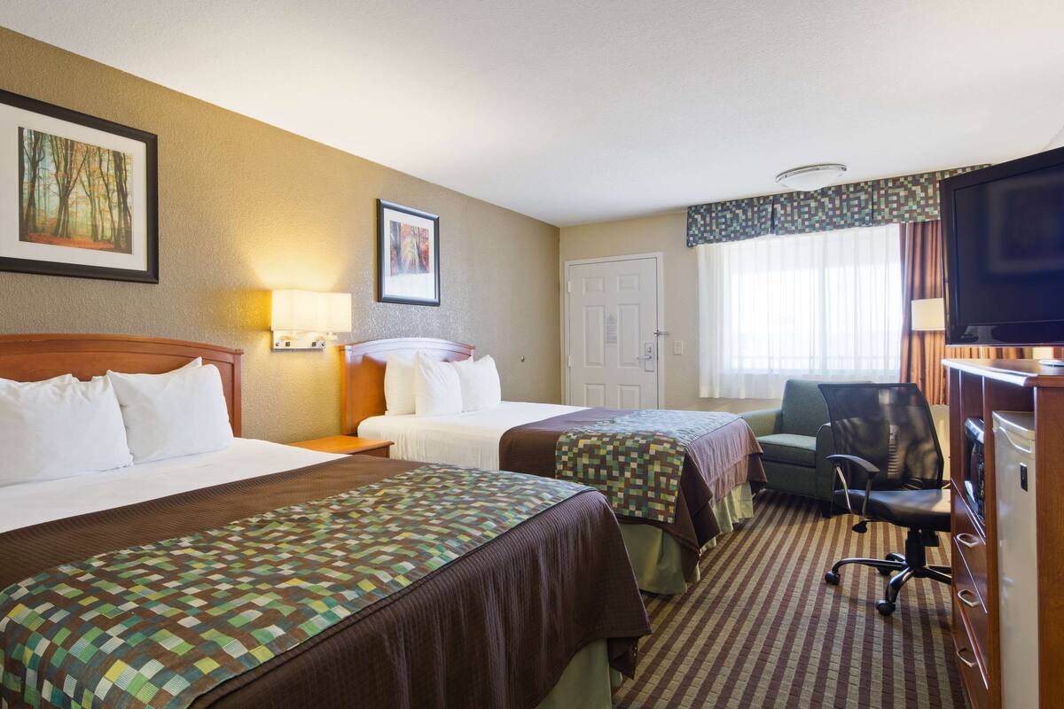 A hotel room with two beds, a desk with a chair, a television, and two framed pictures on the wall.
