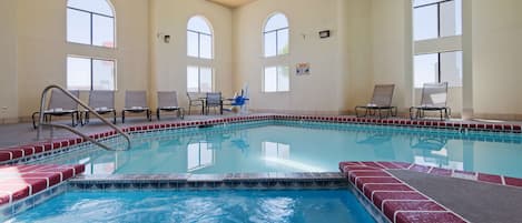 An indoor swimming pool with clear water, surrounded by lounge chairs and a tiled deck.