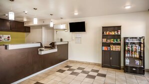 A reception area with a counter, a television mounted on the wall, a refrigerator stocked with beverages, and a vending machine. - Studio 6 Huntsville, TX (Huntsville)
