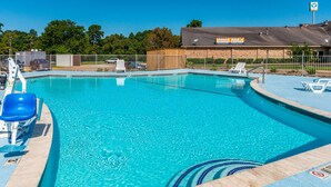 A clear swimming pool with blue water, surrounded by a wooden deck and a fenced area with lounge chairs. - Studio 6 Huntsville, TX (Huntsville)