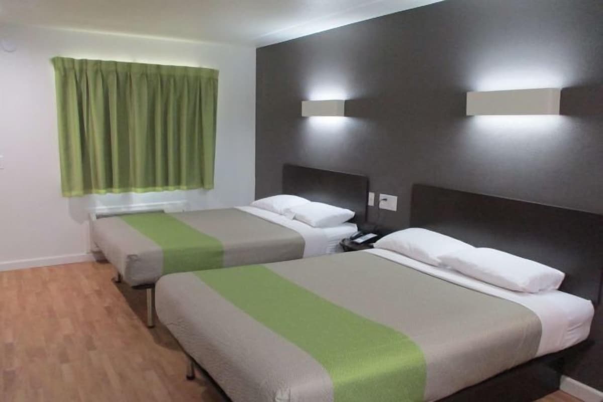 Quarto de hotel com duas camas, cortina verde e luminárias fixadas na parede.