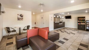 A hotel lobby with a checkered floor, a seating area with brown and red cushions, a small table, and a kitchenette in the background. - Studio 6 Huntsville, TX (Huntsville)