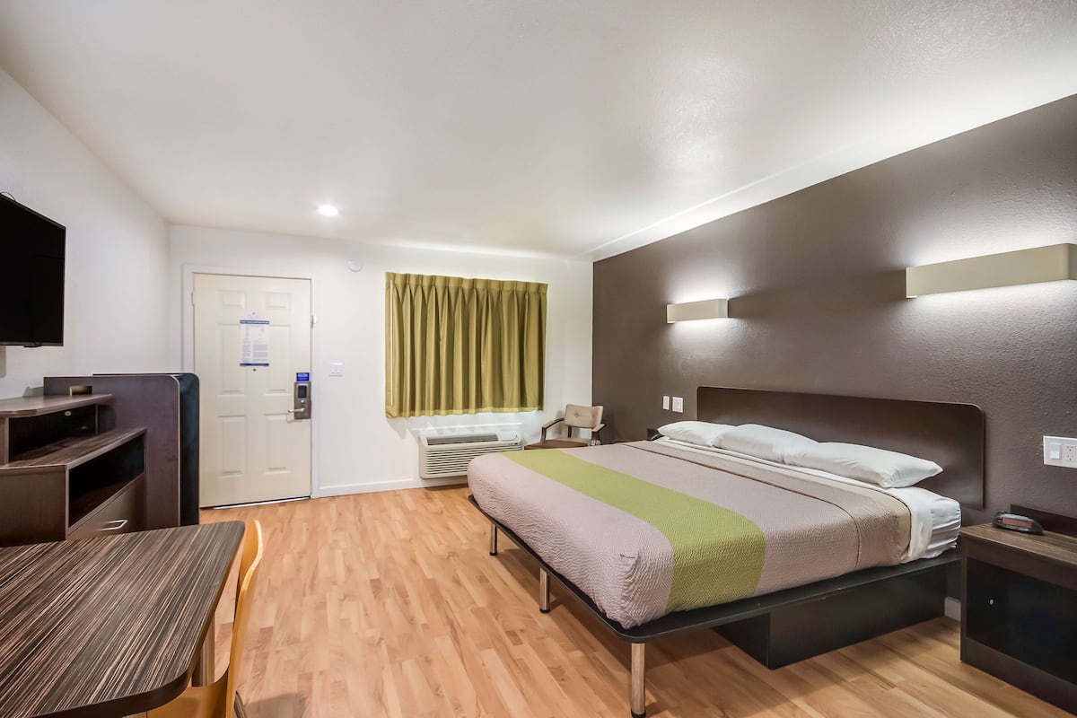 A hotel room with a bed, bedside table, desk, chair, and a television.