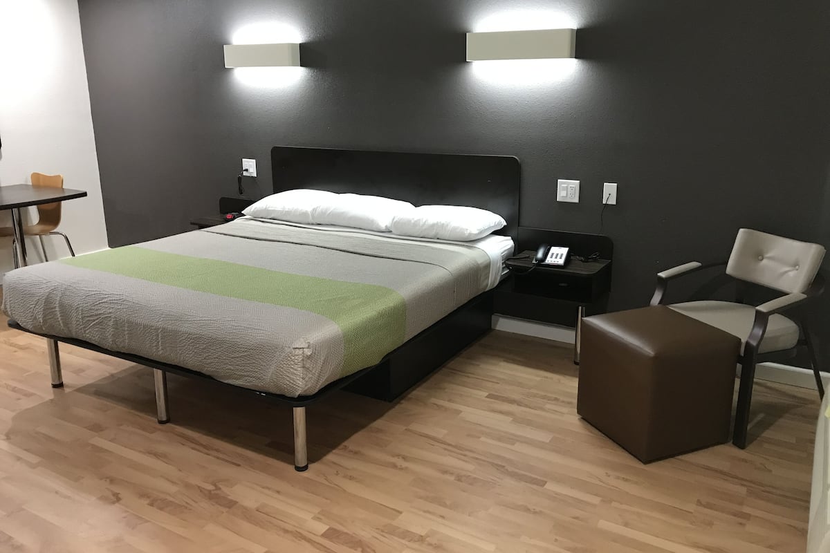A hotel room with a bed, bedside table, chair, and a desk with a chair.