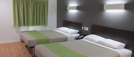 Une chambre d’hôtel avec deux lits, chacun recouvert d’une couvre-lit verte et grise, une table de chevet avec une lampe, et une fenêtre avec des rideaux verts.