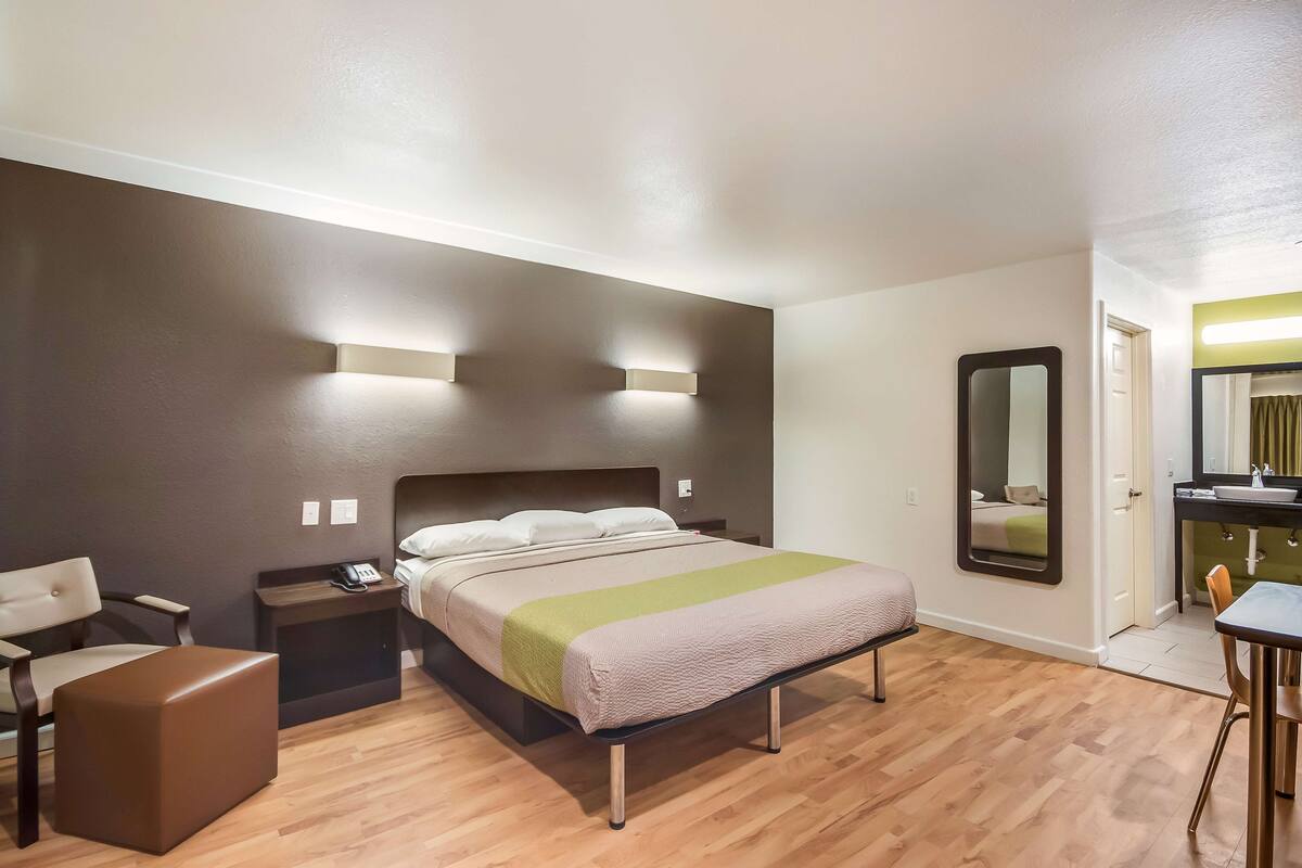 A hotel room with a bed, bedside table, chair, and a small table with a lamp.