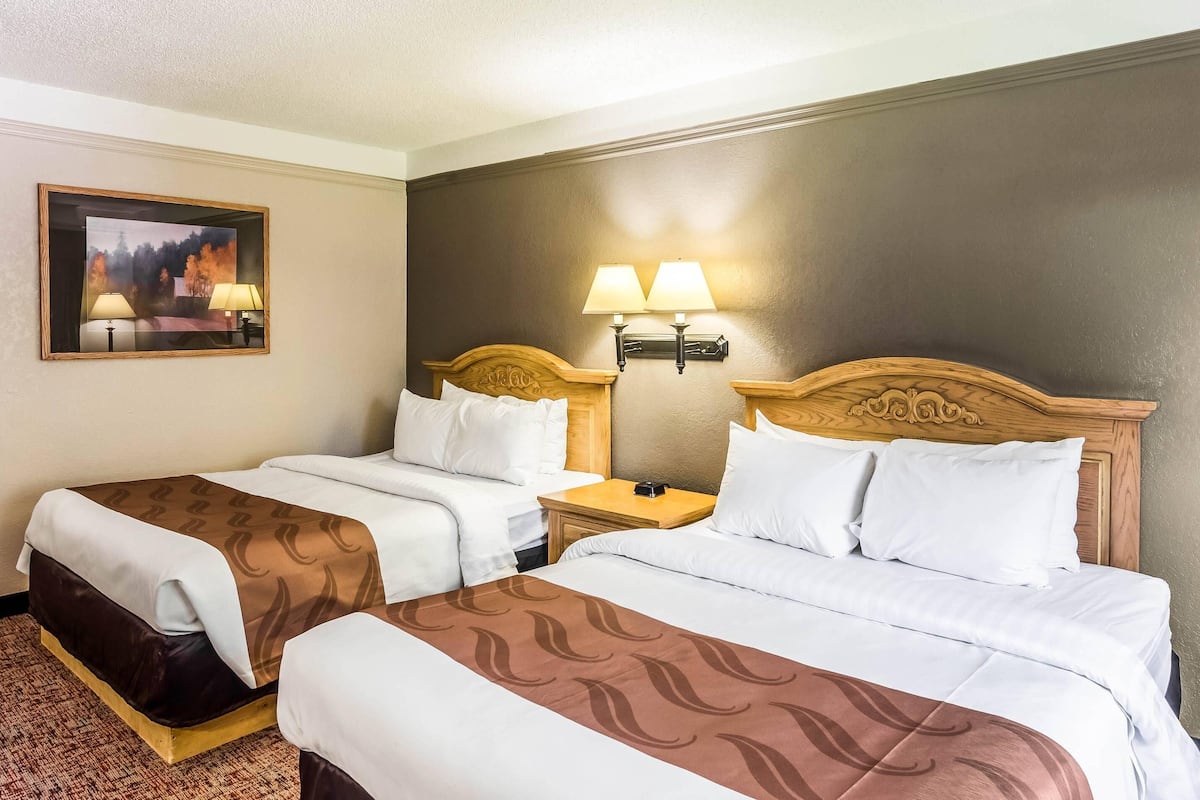 A hotel room with two beds, a painting on the wall, and two bedside lamps.