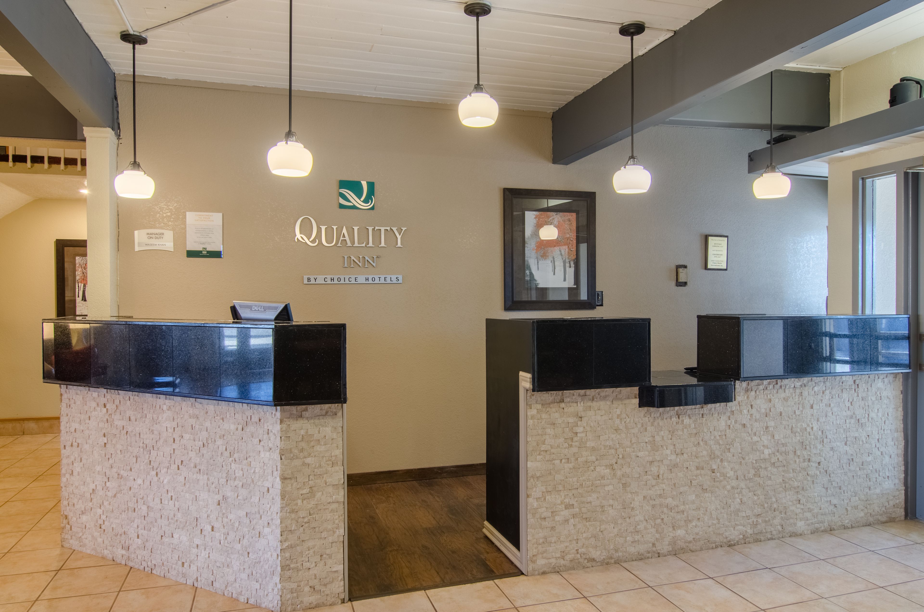 A reception area with two black reception desks, a sign for Quality Inn by Choice Hotels, and pendant lighting.