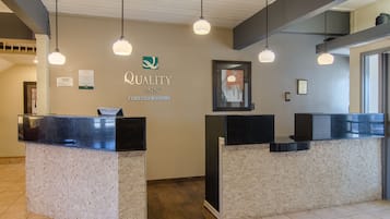 Un área de recepción con dos mostradores negros, un letrero de Quality Inn by Choice Hotels e iluminación colgante.