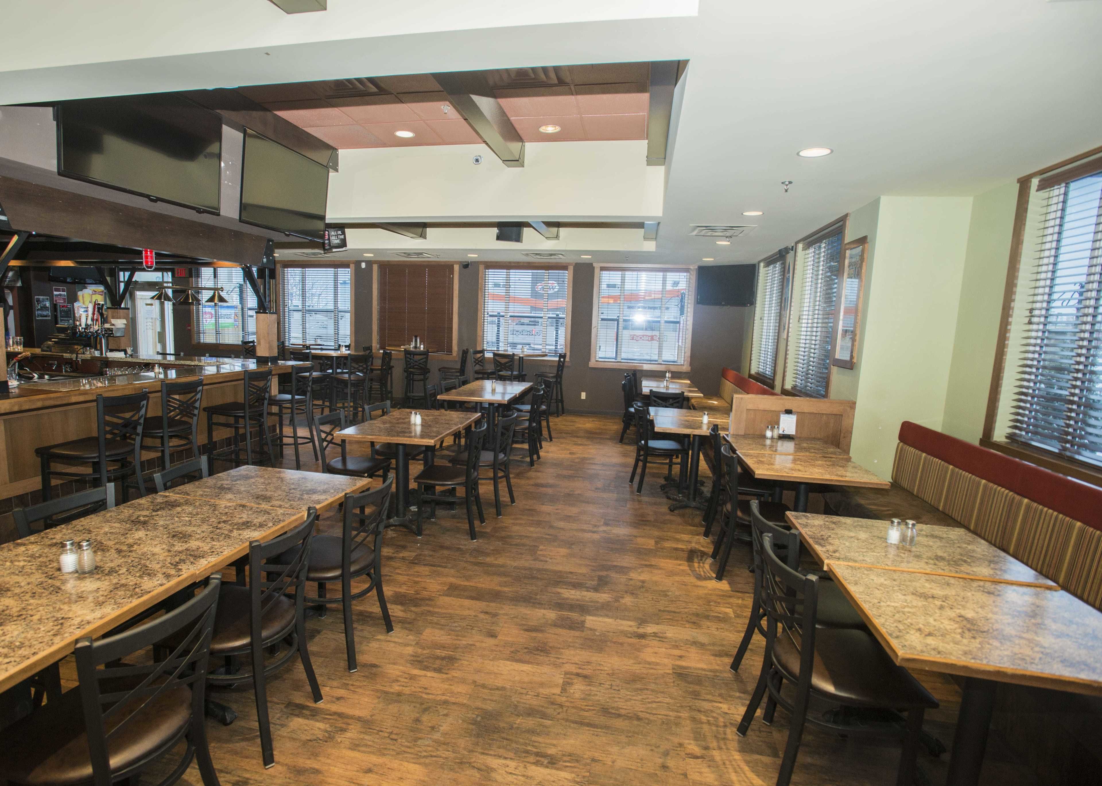 Interior de restaurante con varias mesas y sillas, zona de bar y grandes ventanales.