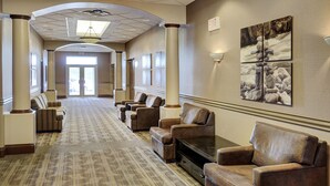 Un vestíbulo de hotel con piso alfombrado, sillones de cuero, un sofá y un televisor de pantalla plana.