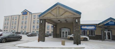 Un hôtel doté d’une entrée couverte, de piliers en pierre et d’un parking où sont garées des voitures.