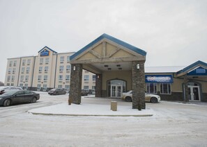 Un hôtel doté d’une entrée couverte, de piliers en pierre et d’un parking où sont garées des voitures.