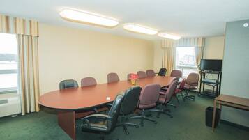 A conference room with a long table, multiple chairs, a television, and a small table with a keyboard.