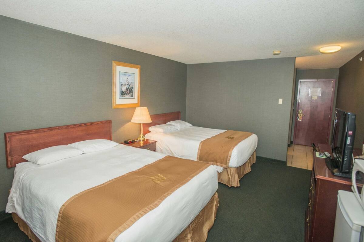A hotel room with two beds, a desk, a television, and a framed picture on the wall.